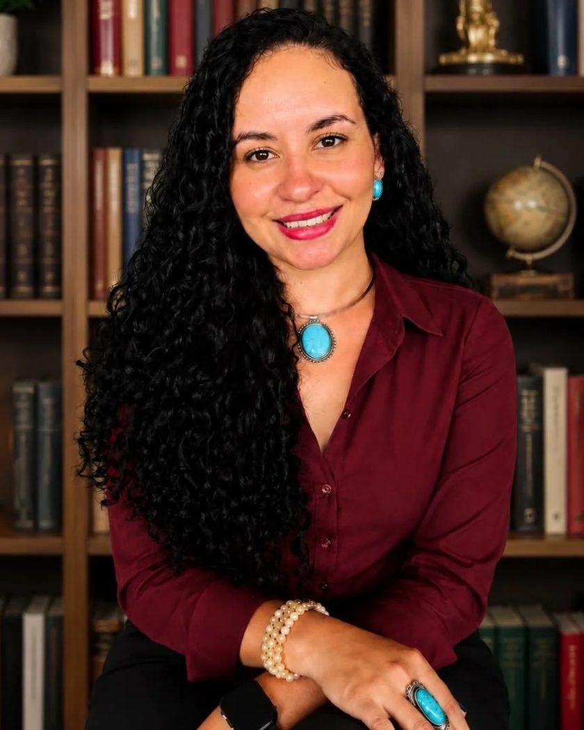 Laiane Andreoleti, psicóloga clínica e supervisora, sentada diante de uma estante de livros em seu consultório.